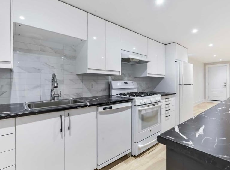 Modern kitchen with white cabinetry, black countertops, stainless steel appliances, and glass backsplash