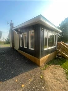 Modern tiny house with dark exterior walls, large windows, and wooden deck foundation on gravel ground