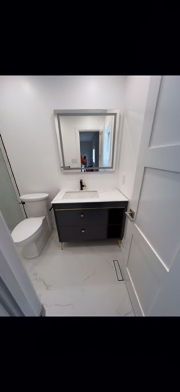Modern bathroom interior with white walls, black vanity with white sink, framed mirror, and white toilet