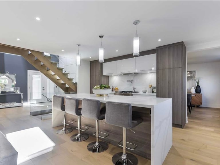 Modern kitchen and dining area with white island, bar seating, pendant lighting, and wooden staircase in background
