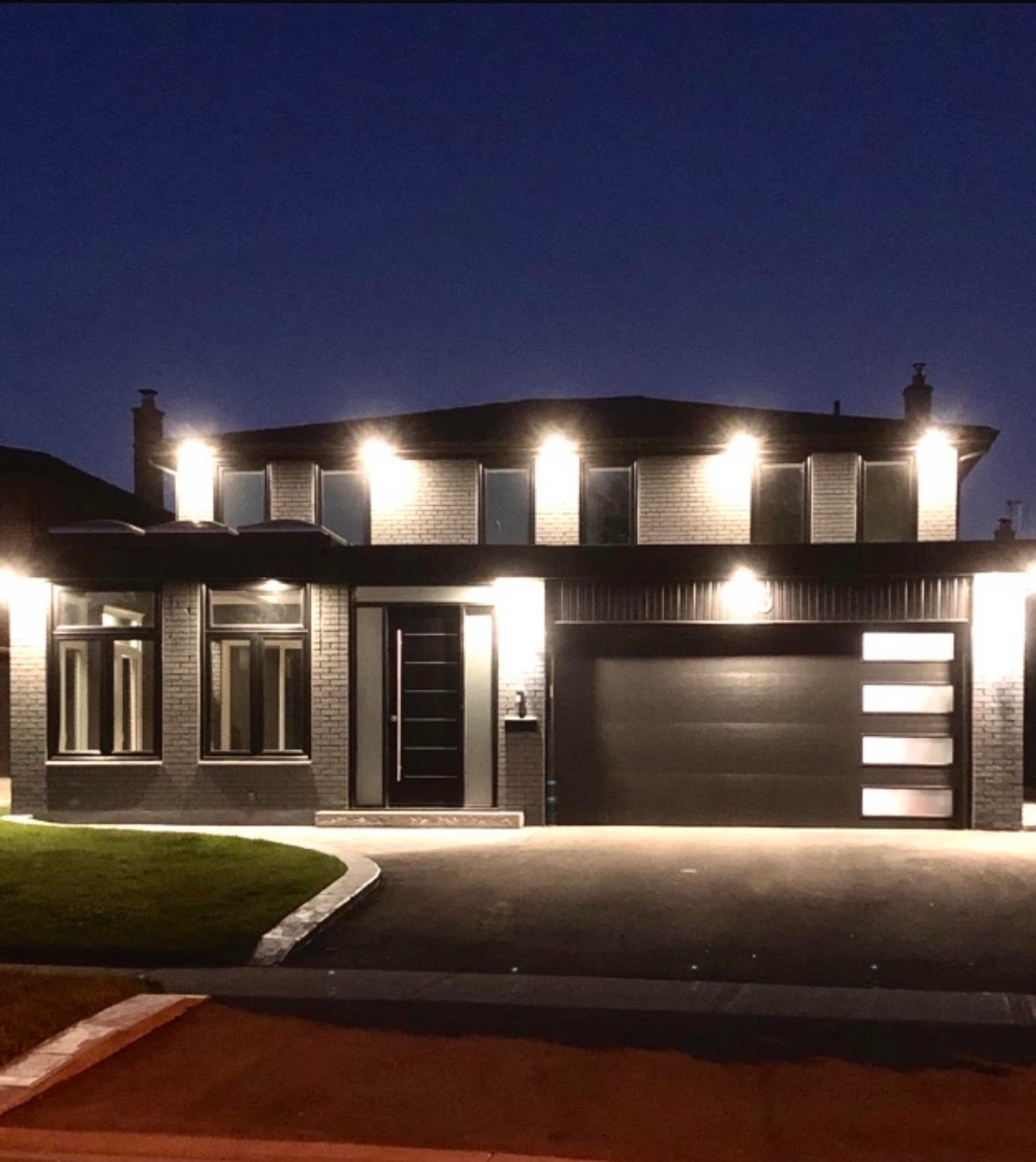 Modern two-story brick house illuminated at night with landscaped lawn and black garage door