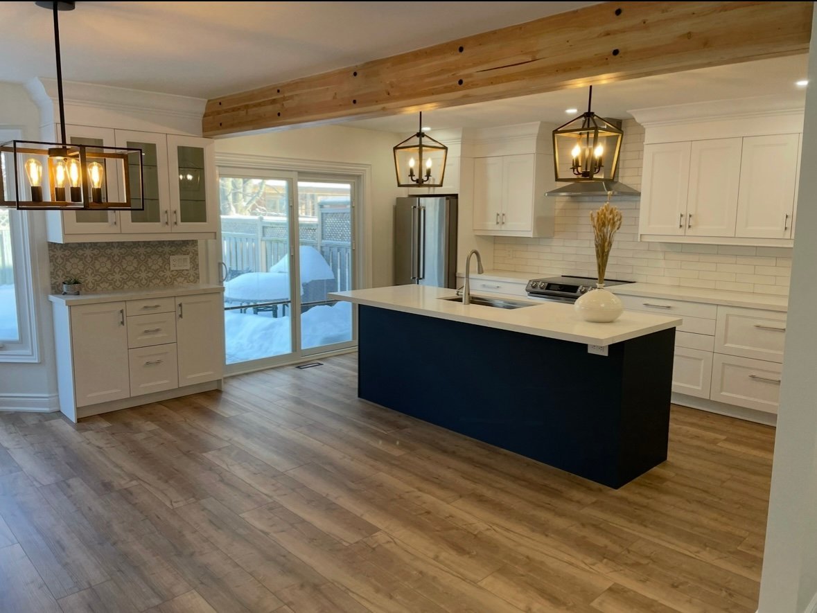 Modern kitchen with white cabinetry, black island, wood beam ceiling, pendant lights, and hardwood floors with glass door to patio