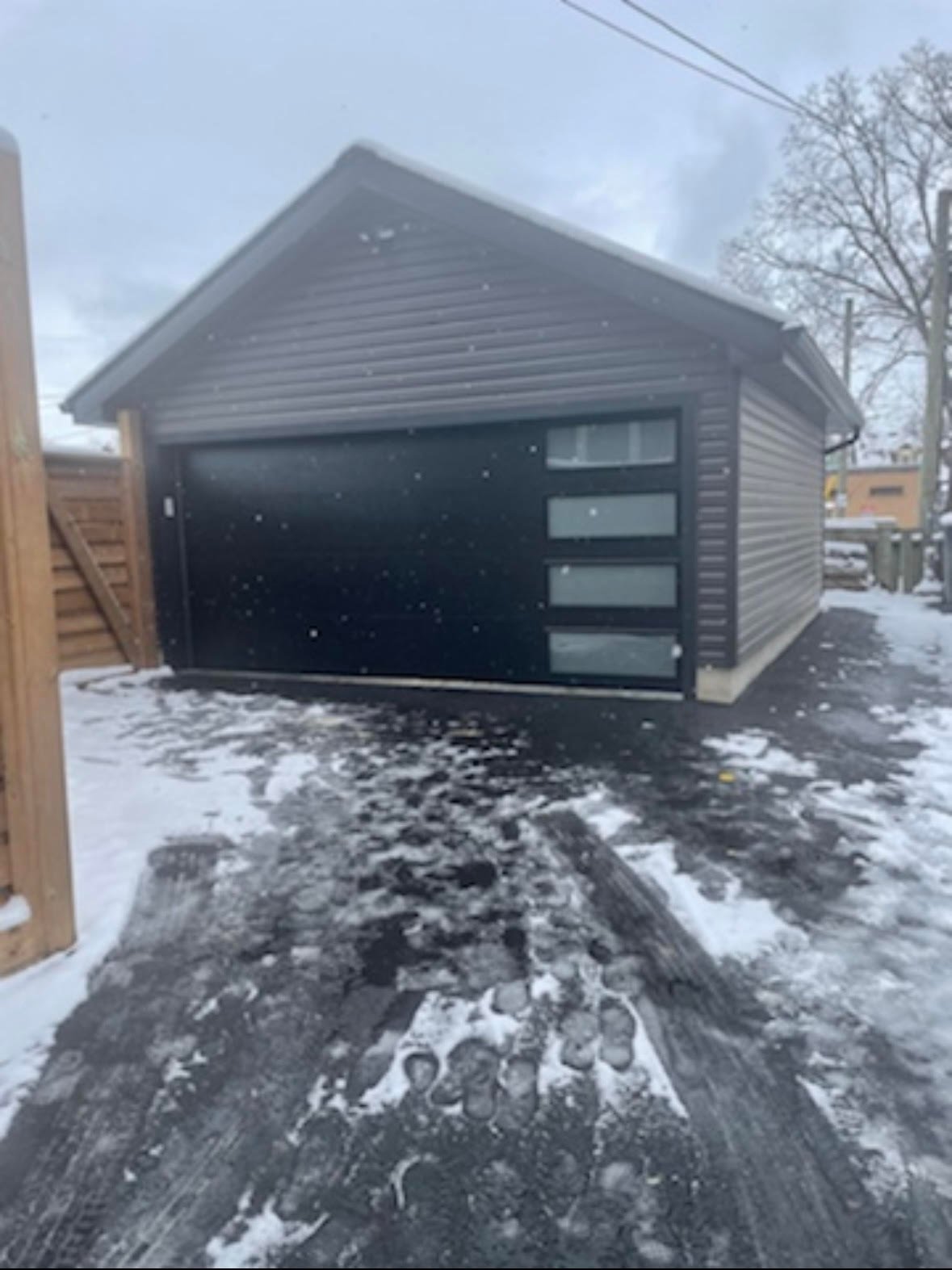Modern black garage with horizontal windows in snowy winter setting, attached to residential property