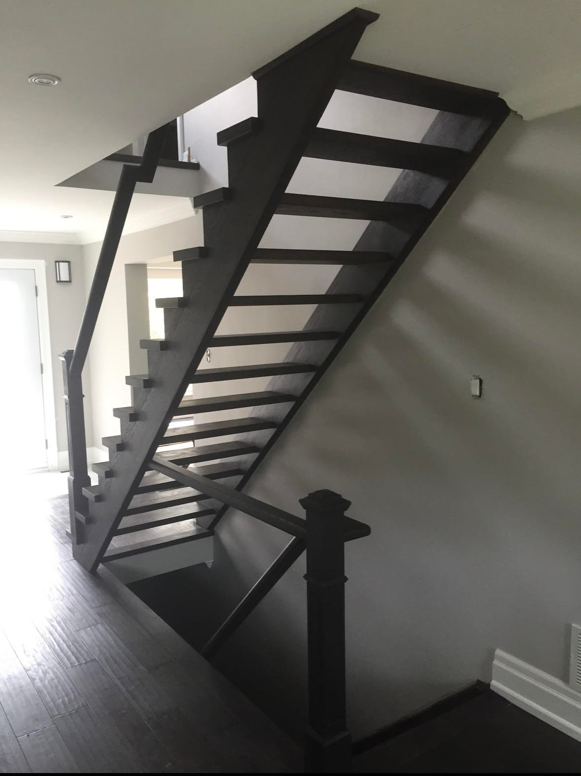 Modern black metal staircase with light wood steps ascending against a white wall in an interior space