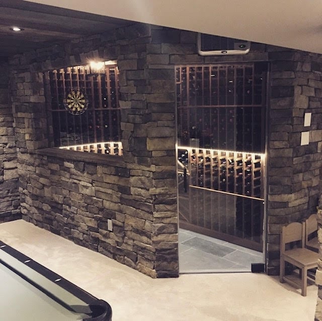 Modern wine cellar with dark stone walls, metal gates, and ambient lighting displaying wine bottles on illuminated shelves
