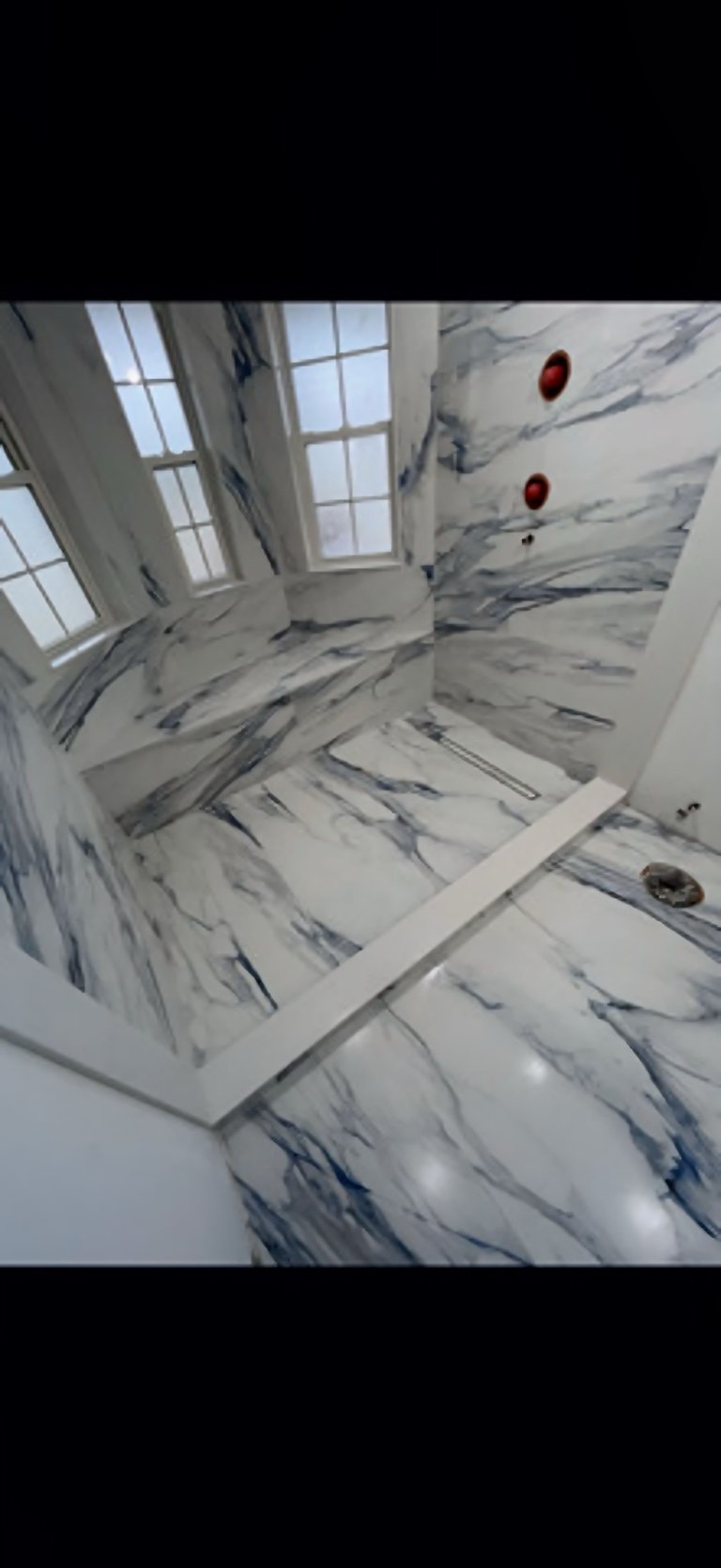 Interior overhead view of modern bathroom with marble-textured walls, skylight window, and red circular fixtures on white surfaces