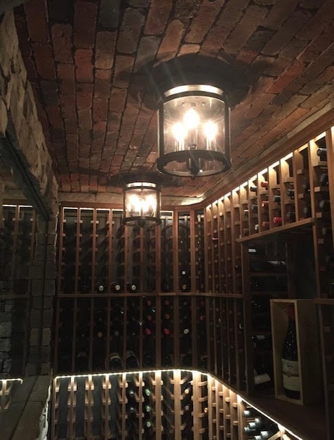 Wine cellar with brick arched ceiling, floor-to-ceiling wooden wine racks, and hanging pendant lights illuminating rows of wine bottles