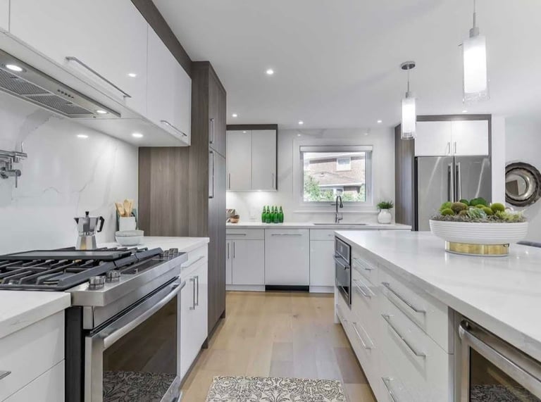 Modern kitchen with white cabinetry, stainless steel appliances, white quartz countertops, and wooden flooring.