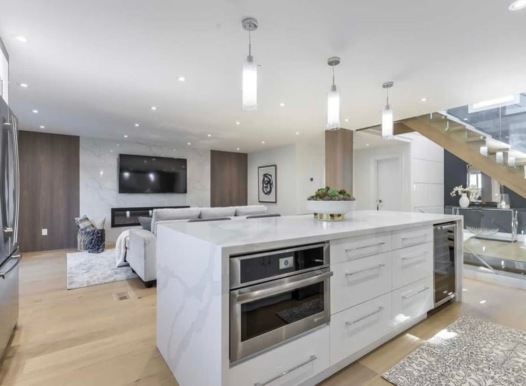 Modern kitchen with white marble island, stainless steel appliances, pendant lights, and open living area with wood flooring