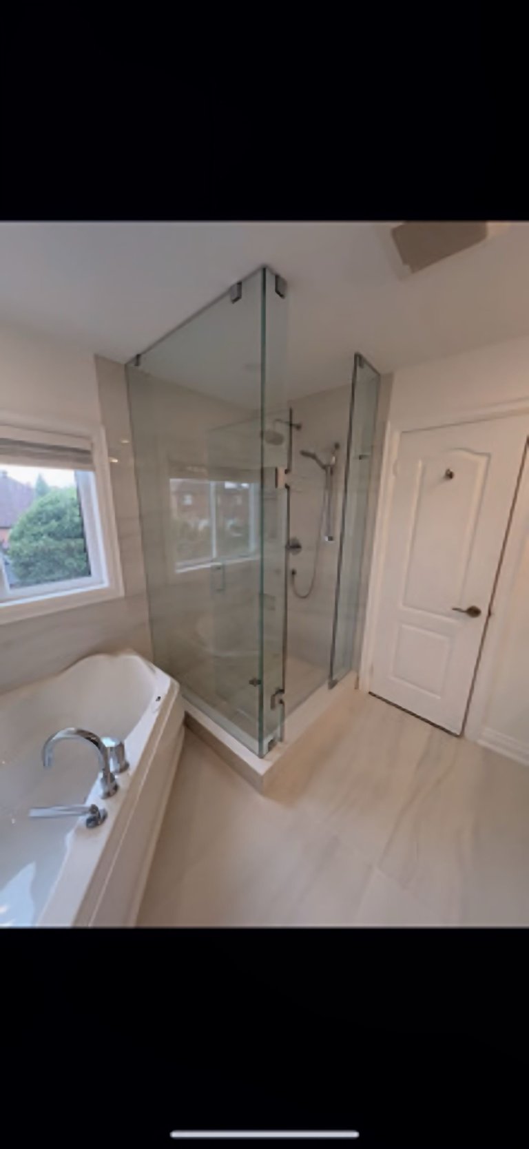 Modern bathroom with glass-enclosed shower enclosure, white bathtub on left, and white door on right wall