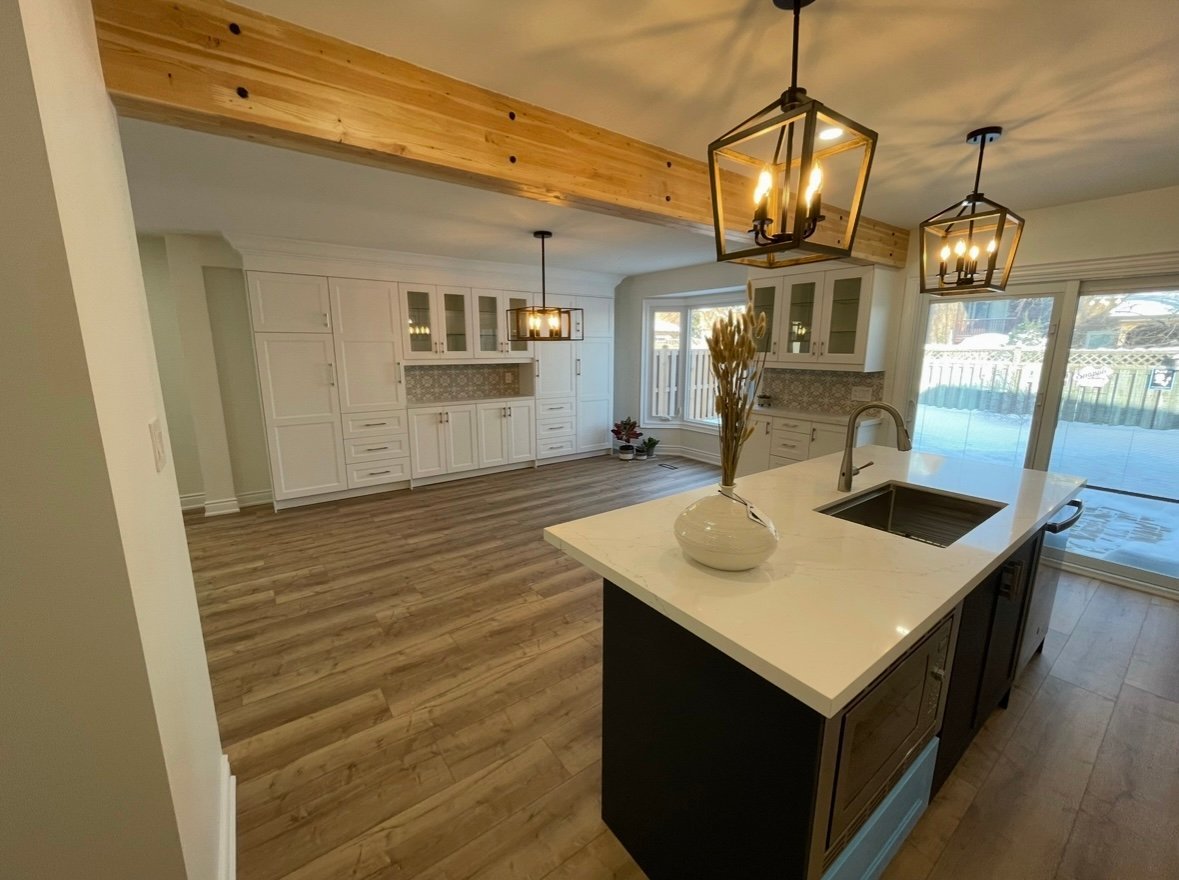Modern kitchen with large island, white cabinetry, wood beams, pendant lighting, and views to patio