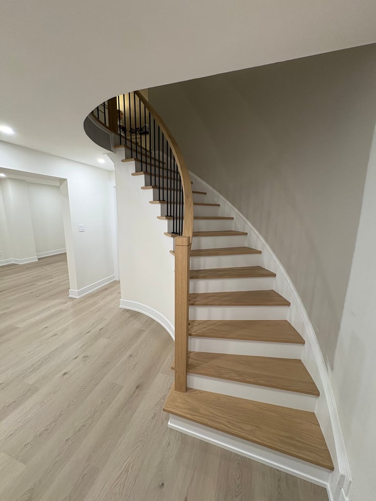 Modern curved staircase with wooden treads and black metal railing in bright interior space with light wood flooring