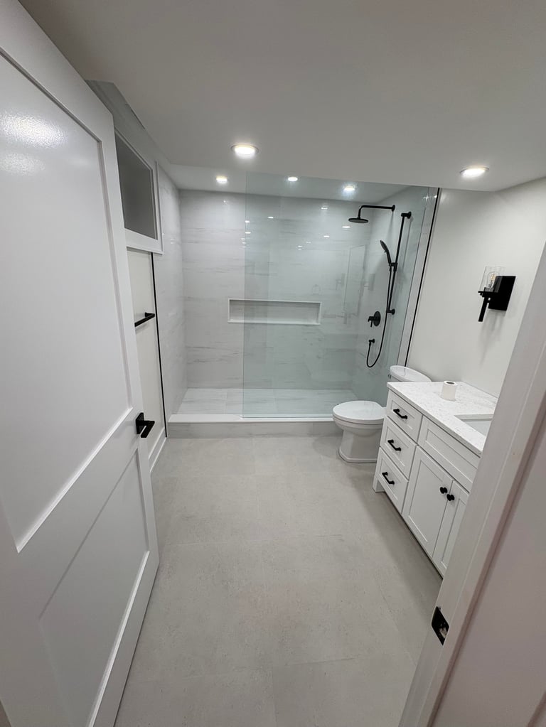 Modern bathroom with white cabinetry, glass shower enclosure, toilet, and marble flooring